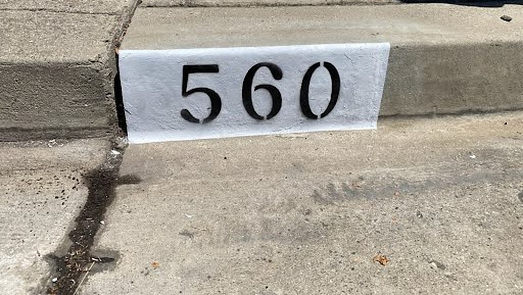 Freshly painted curb with black stenciled house number 560 on a clean white block